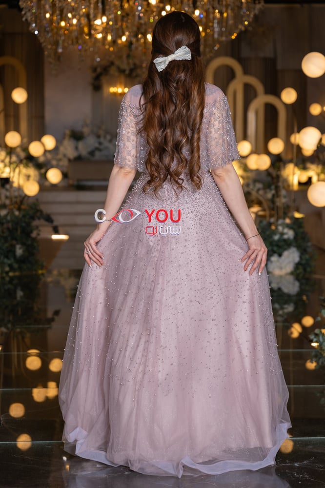 A pink evening dress embroidered with delicate beads and a short sheer cape adds a dreamy, feminine touch, perfect for engagements and luxurious occasions.