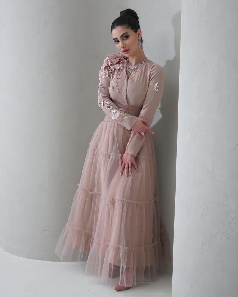 Elegant and soft dress in a nude color with a pinkish tint, decorated with embroidery on the shoulder, long sleeves, with a wide belt at the waist to shape the body, made of Barbie fabric and tulle from Jawhara store
