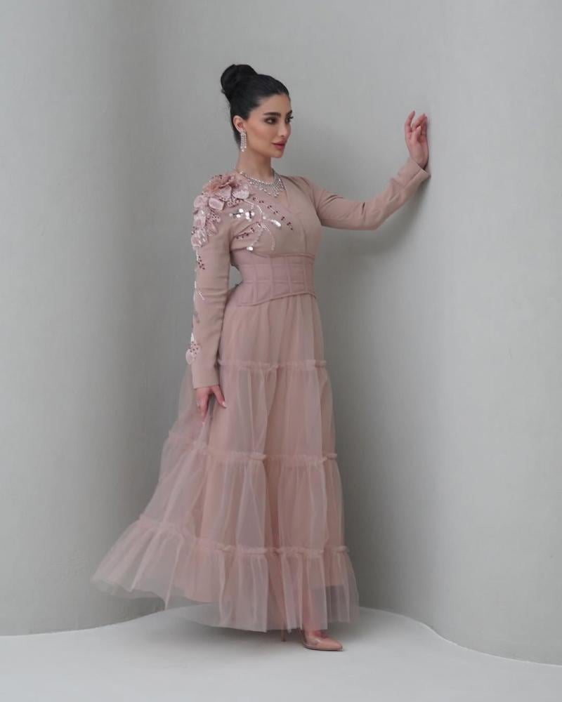 Elegant and soft dress in a nude color with a pinkish tint, decorated with embroidery on the shoulder, long sleeves, with a wide belt at the waist to shape the body, made of Barbie fabric and tulle from Jawhara store