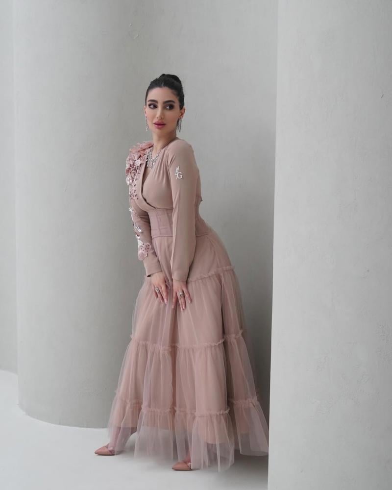 Elegant and soft dress in a nude color with a pinkish tint, decorated with embroidery on the shoulder, long sleeves, with a wide belt at the waist to shape the body, made of Barbie fabric and tulle from Jawhara store