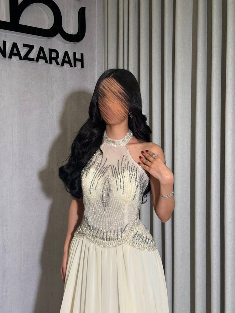 فستان كامل بصدر من التل المطرز بالخرز والكريستال، مع خصر محدد وجزء سفلي من الشيفون بكسرات ناعمة وانسيابية