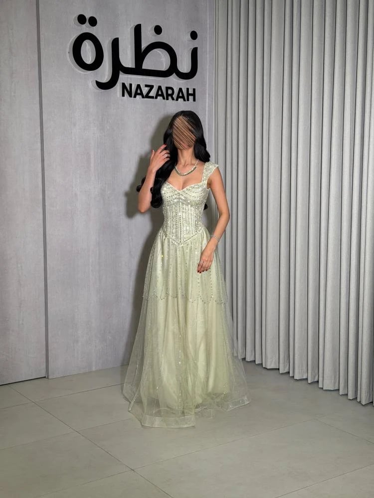 فستان سهرة بقصة كورسيه محددة للخصر، مزين بتطريز كثيف من الخرز والكريستال، مع طبقات من التل المطرز من الأسفل.