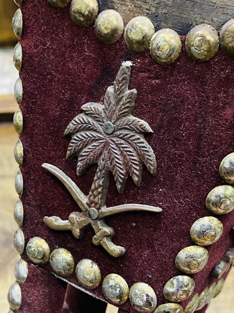 من النوادر؛ مبخرة خشبية بطول ٢٥سم؛ مغطاة بقطيفة لون عنابي غامق ومزينة بالقمور وتحمل شعار سيفين ونخلة و المملكة العربية السعودية على قطع نحاسية