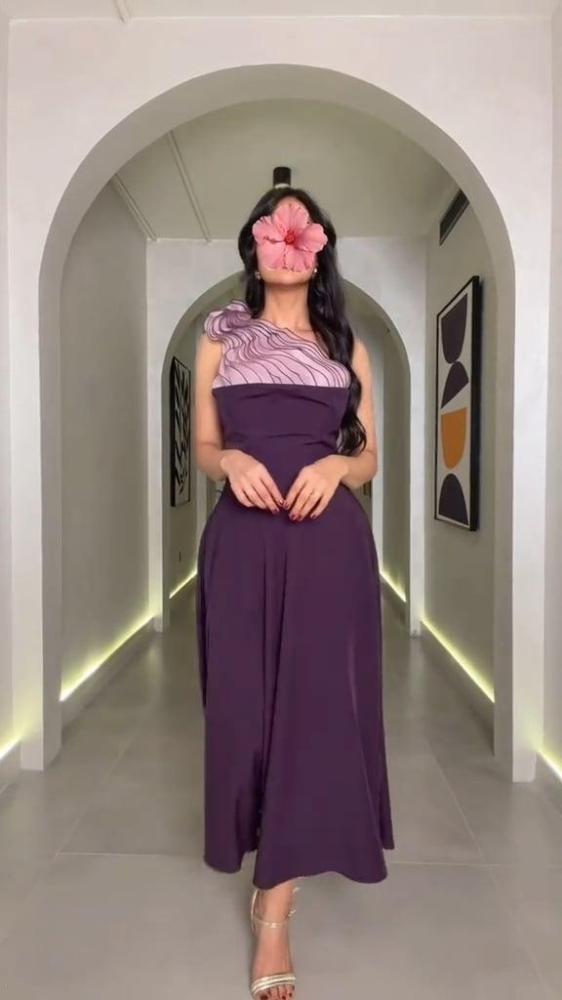 فستان منفرد أنيق بلون بنفسجي غامق، بتصميم كتف واحد وتفصيل زخرفي ناعم باللون الليلكي، مع تنورة واسعة تمنح انسيابية وحركة راقية.
