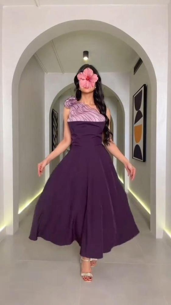 فستان منفرد أنيق بلون بنفسجي غامق، بتصميم كتف واحد وتفصيل زخرفي ناعم باللون الليلكي، مع تنورة واسعة تمنح انسيابية وحركة راقية.