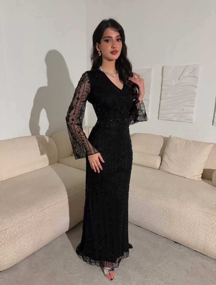 فستان أسود فاخر بتطريزات خرز لامعة متدرجة، وأكمام شفافة، مع تنورة دانتيل طويلة وانسيابية