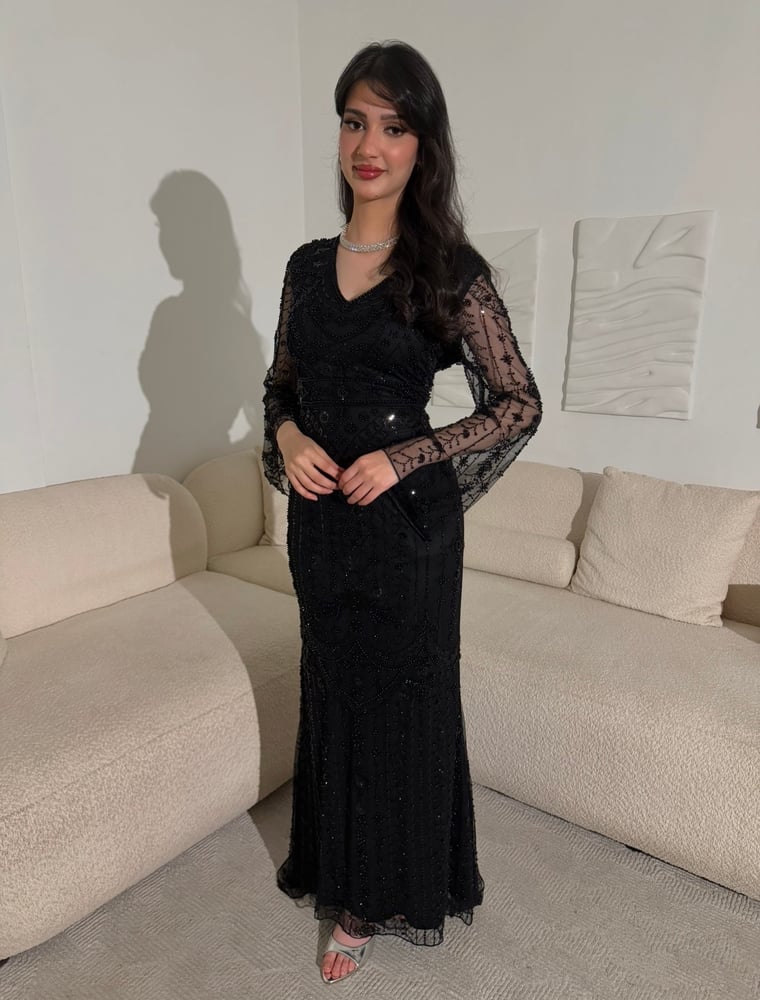 فستان أسود فاخر بتطريزات خرز لامعة متدرجة، وأكمام شفافة، مع تنورة دانتيل طويلة وانسيابية