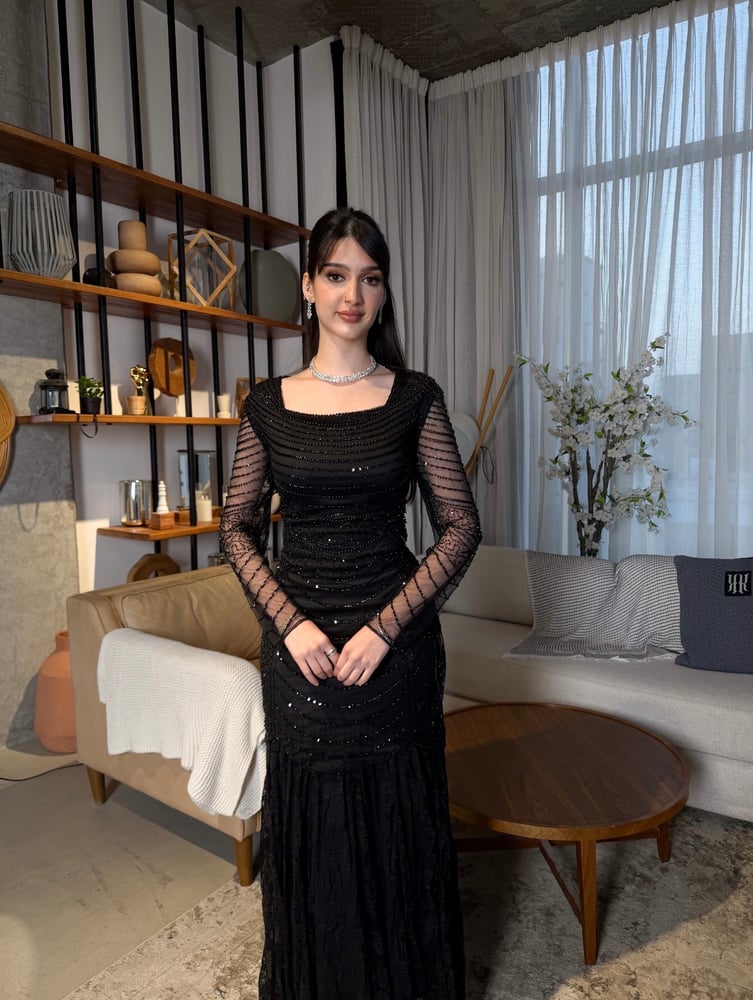 فستان أسود فاخر بتطريزات خرز لامعة متدرجة، وأكمام شفافة، مع تنورة دانتيل طويلة وانسيابية