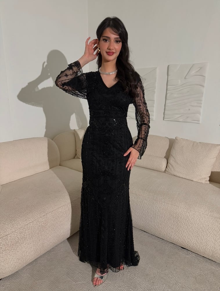 فستان أسود فاخر بتطريزات خرز لامعة متدرجة، وأكمام شفافة، مع تنورة دانتيل طويلة وانسيابية