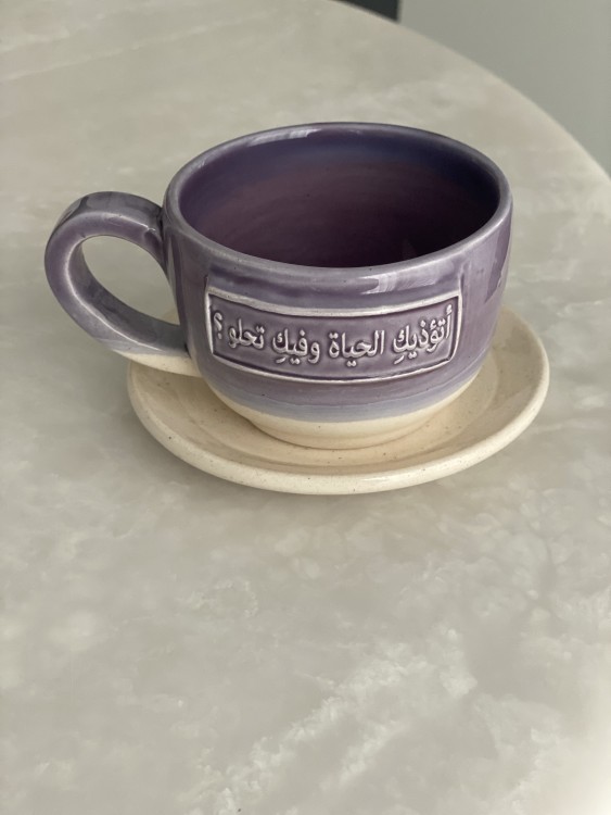 كوب مع طبق بعبارة ( أتؤذيكِ الحياة وفيكِ تحلو؟)