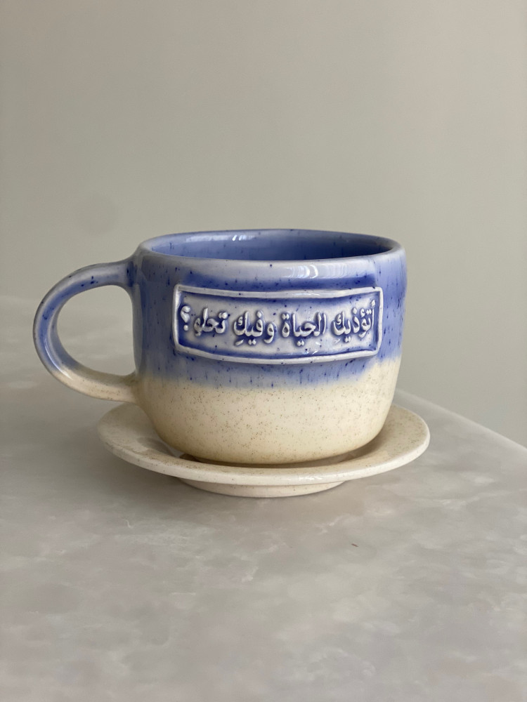 كوب بعبارة ( أتؤذيكِ الحياة وفيكِ تحلو ؟)