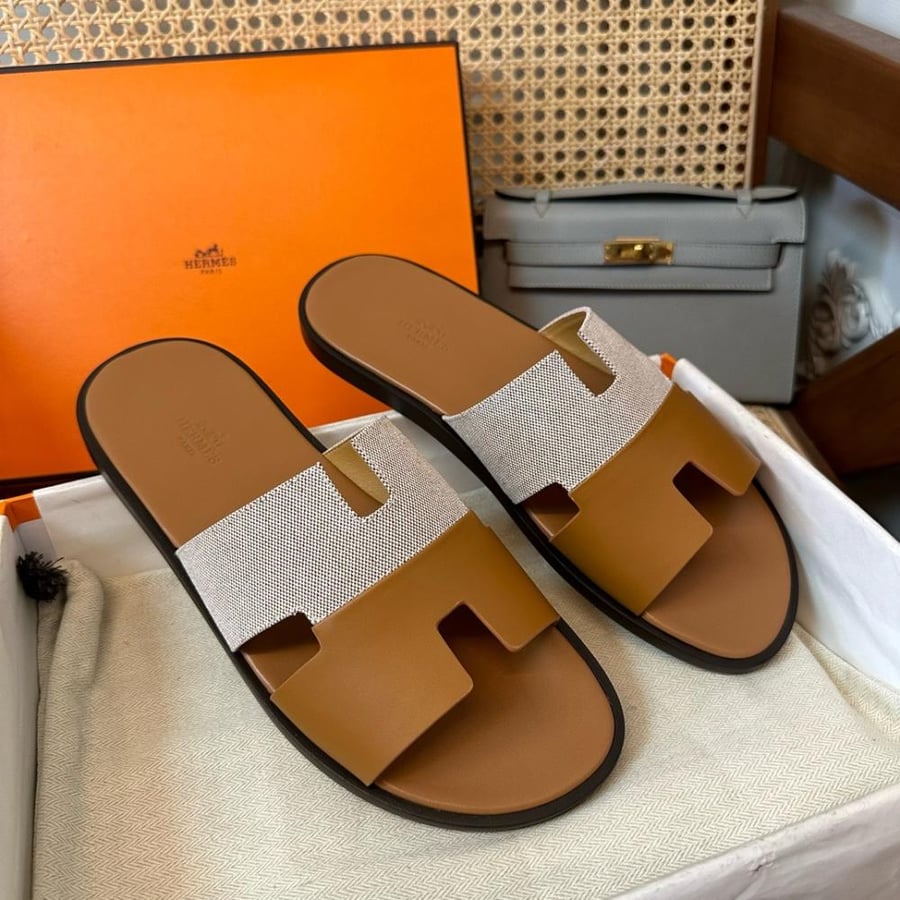 نعال إيزمير (Izmir) الصيفي الفاخر من هرمز (Hermès) بمزيج الجلد الطبيعي والقماش باللونين الهافان والرمادي الفاتح.