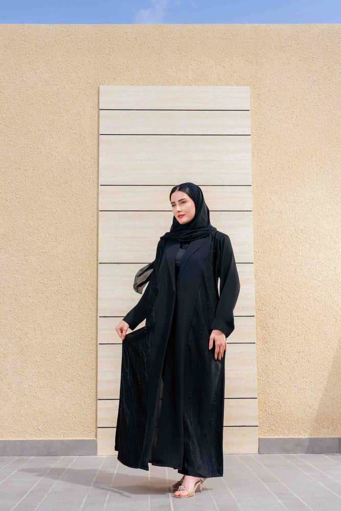 عباية رُبى سوداء بتصميم أنيق وهادئ، تتميز بقصة طويلة وانسيابية