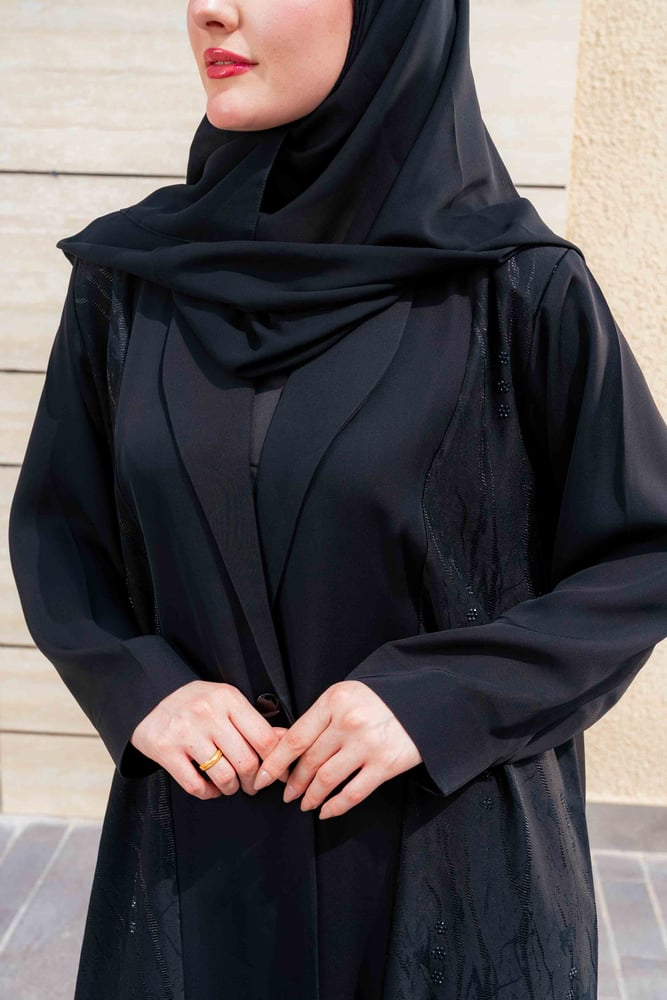 عباية رُبى سوداء بتصميم أنيق وهادئ، تتميز بقصة طويلة وانسيابية