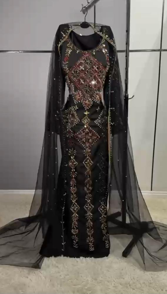 مخور أسود من قماش كريب ناعم، مزين بتطريز يدوي وأحجار لامعة بالأحمر والذهبي، مع رداء تول شفاف طويل يمنحه إطلالة ملكية أنيقة ومميزة.