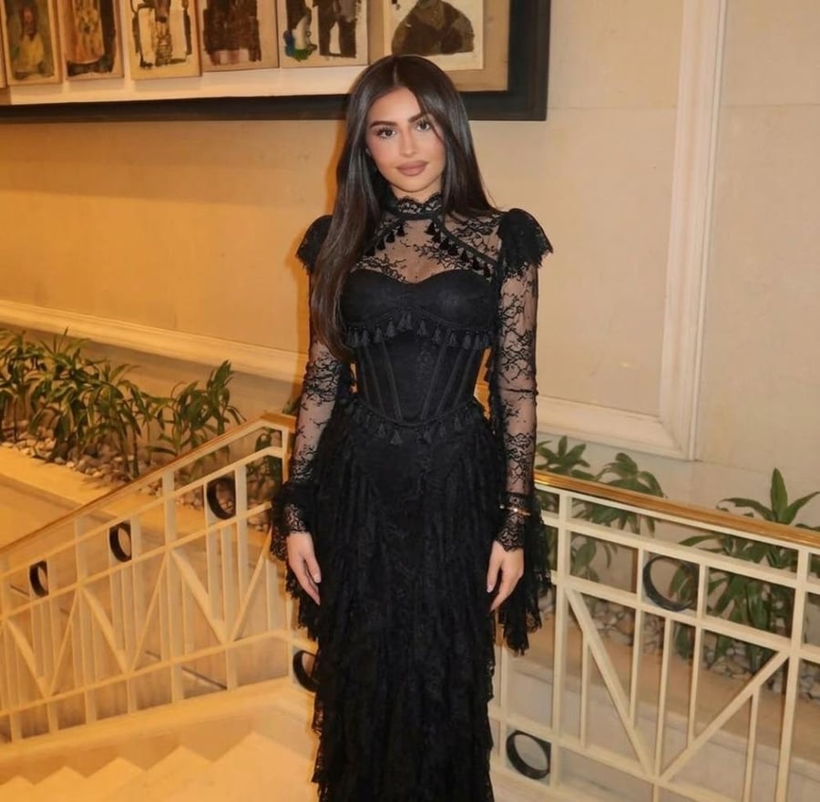 فستان سهرة أسود فاخر بياقة مرتفعة وأكمام من الدانتيل الشفاف، يتزين بقَصّة كورسيه أنيقة للخصر وتنورة طبقات متدرجة غنية بالشراشيب.