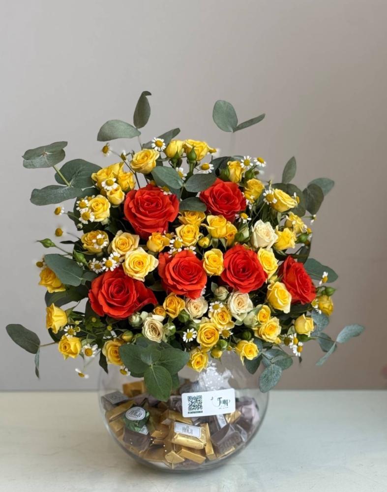 A kilogram of chocolate rolls with a vase of roses