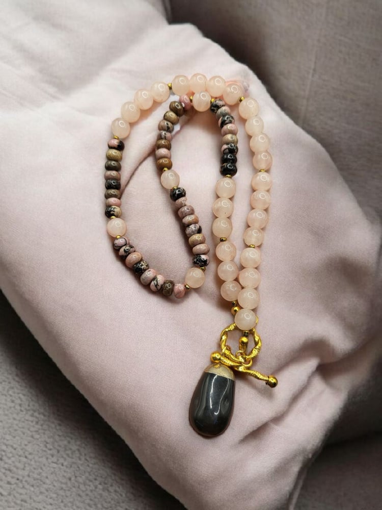 A necklace of femininity stone rose quartz with a stone of rhodonite and decorated with a piece of black onyx stone.