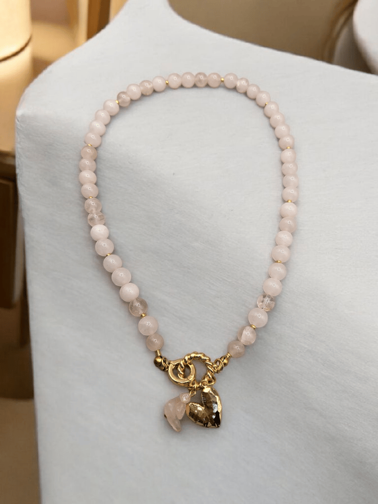 A necklace of rose quartz stone enhanced for femininity with a gold-plated charm