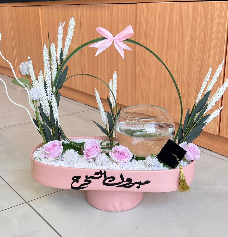 تنسيق يدمج بين حوض سمك زجاجي دائري وقاعدة ورد متكاملة.
