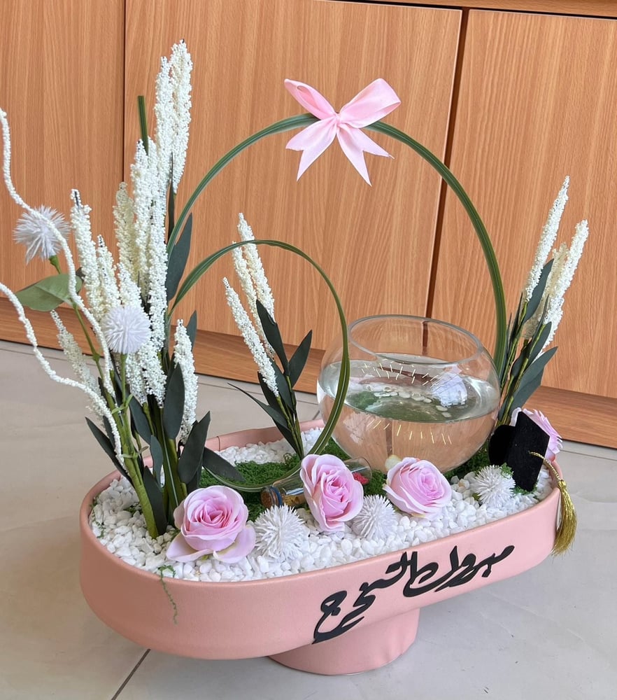 تنسيق يدمج بين حوض سمك زجاجي دائري وقاعدة ورد متكاملة.