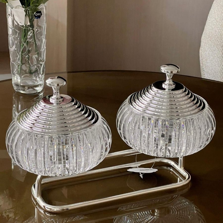 Elegant serving set consisting of two glass bowls with lids connected by a metal holder