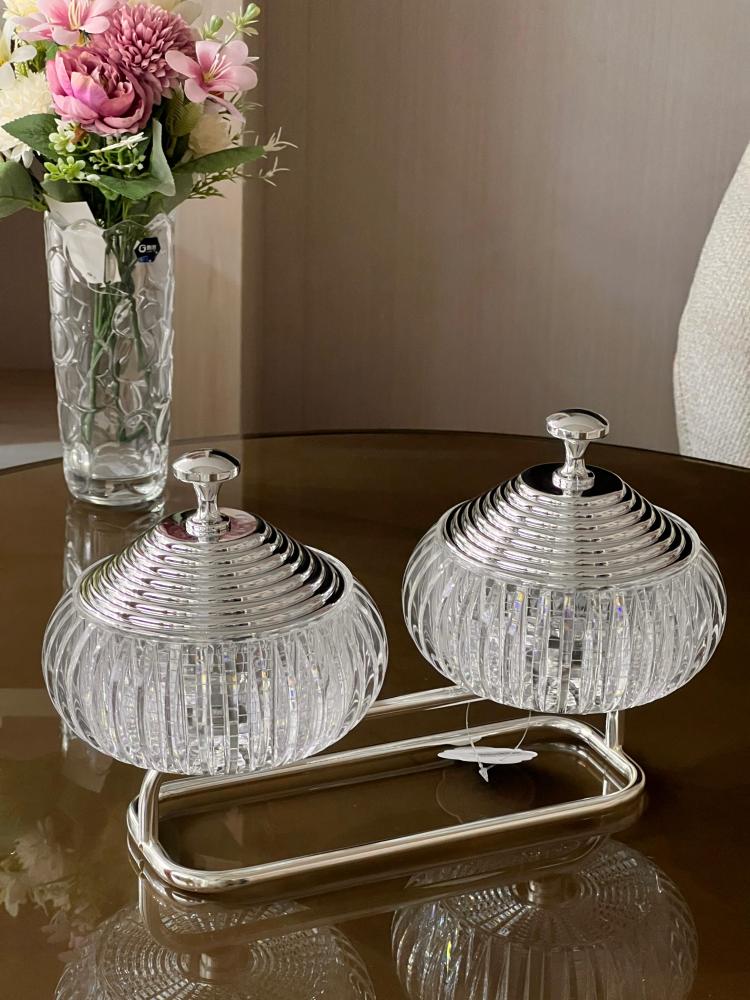 Elegant serving set consisting of two glass bowls with lids connected by a metal holder