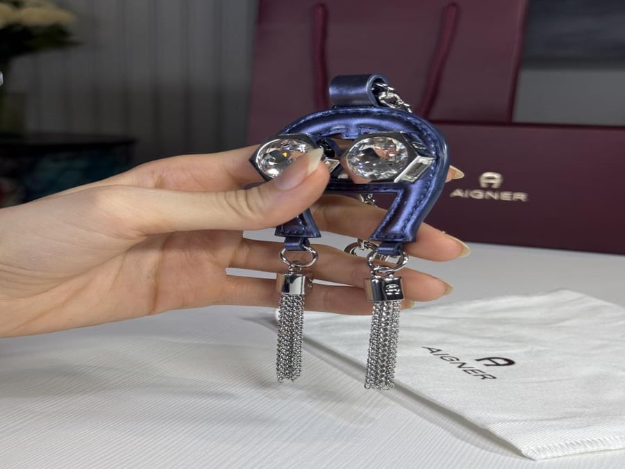 تعليقة اجنر باللون الازرق المعدني اللامع على شكل حذوه من الجلد الوردي Aigner metallic blue charm with stones and tassel's