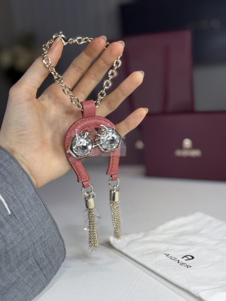 تعليقة اجنر باللون الوردي المرصع بالاحجار على شكل حذوه من الجلد الوردي Aigner pink charm with stones and tassels