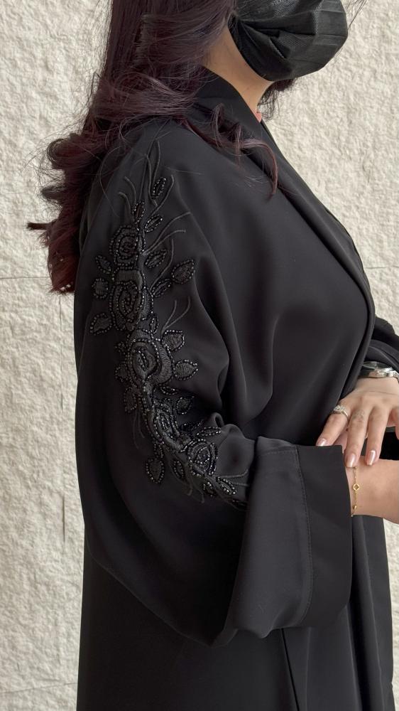 تفاصيل تطريز زهري أسود لامع على كم عباية كلوش سوداء