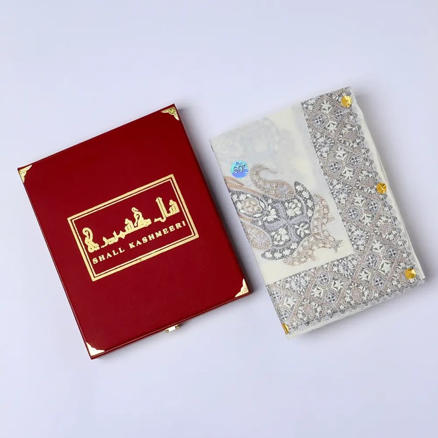 شال كشميري رجالي أوف وايت بتطريز رمادي فضي وبيج بجانب علبة هدايا حمراء