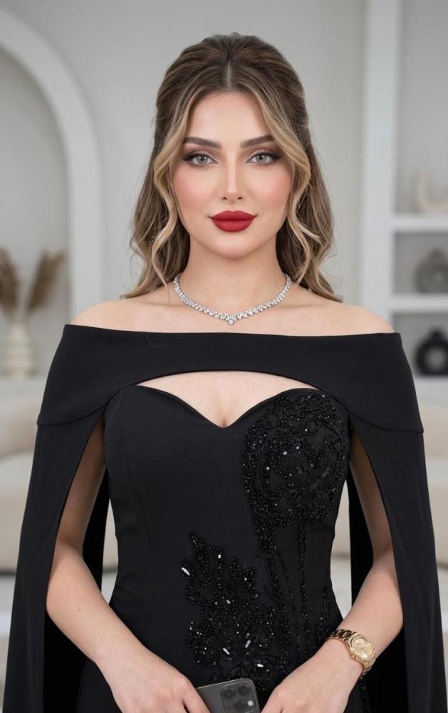 فستان سهرة أسود طويل يتميز بتصميم "أوف شولدر" مع تطريز لامع على الصدر والخصر، ويكتمل بأكمام كاب منسدلة أنيقة