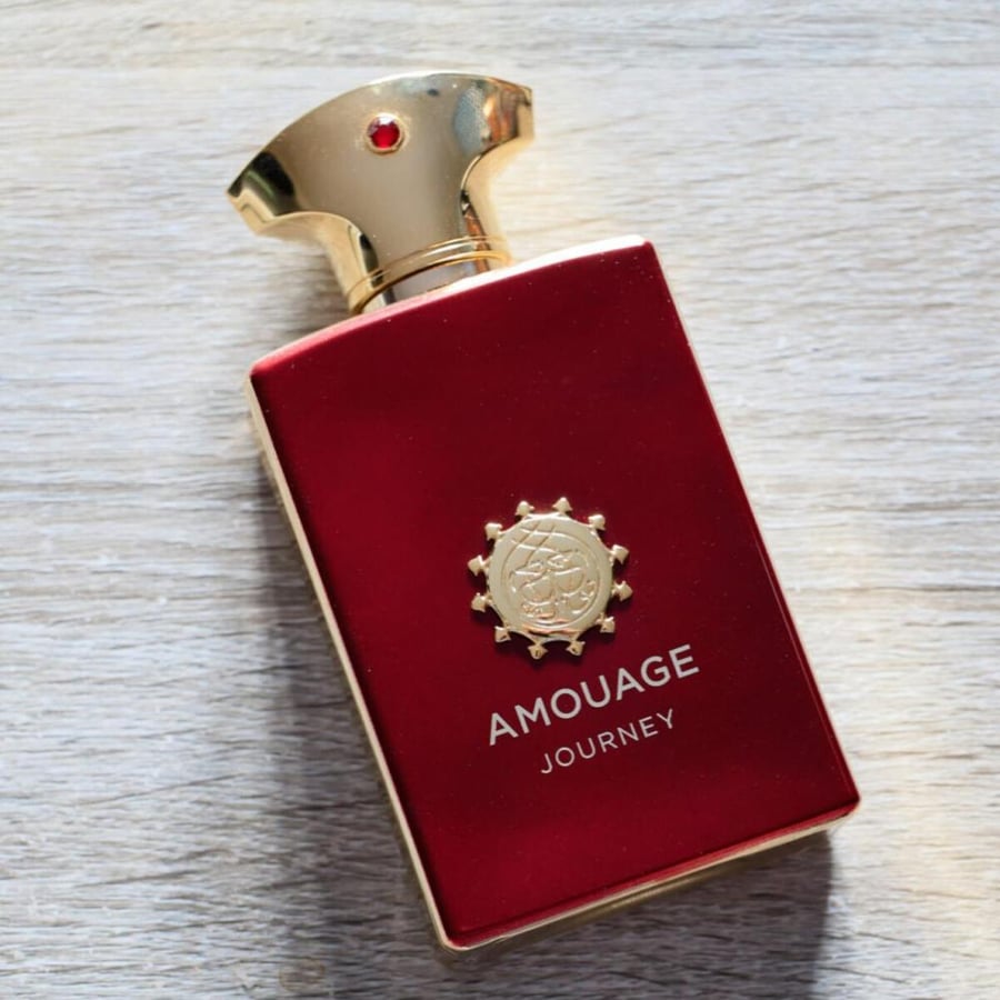 زجاجة عطر أمواج جورني مان الحمراء بغطاء ذهبي مائلة على سطح خشبي فاتح