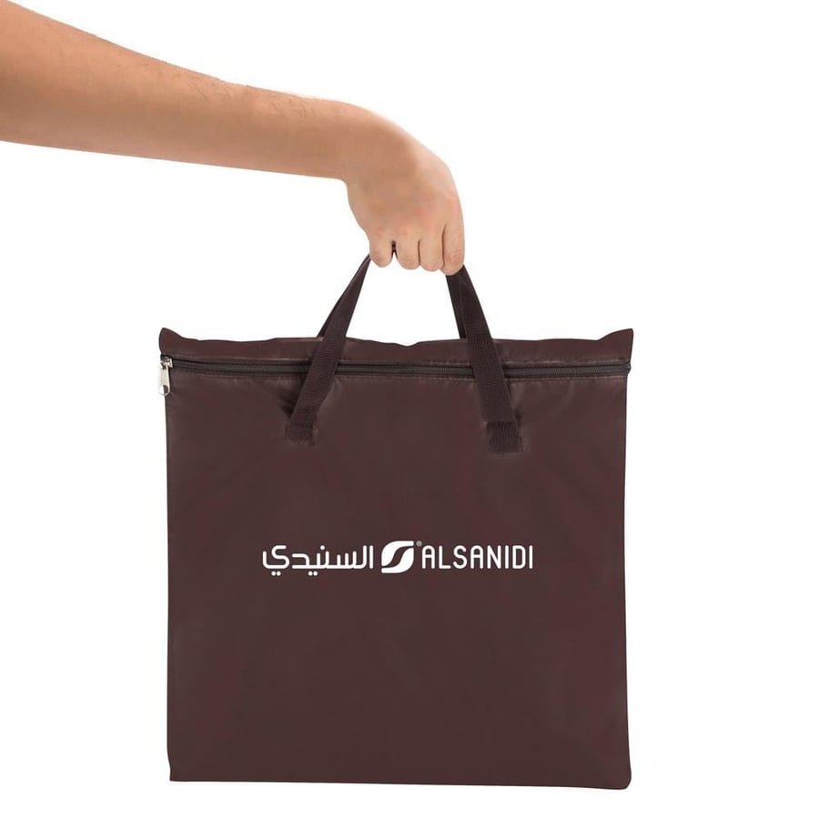 يد تحمل حقيبة بنية اللون بشعار السنيدي تظهر في زاوية علوية مع سحاب