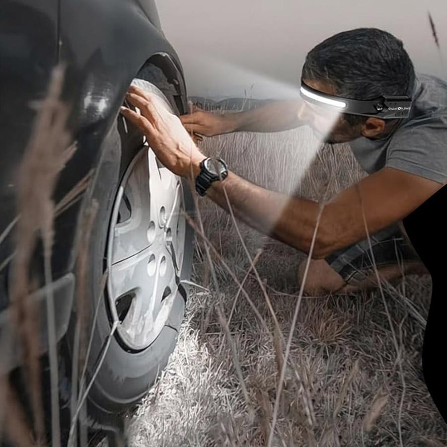 شخص يستخدم كشاف رأس LED من السنيدي لإضاءة منطقة إطار السيارة ليل ا