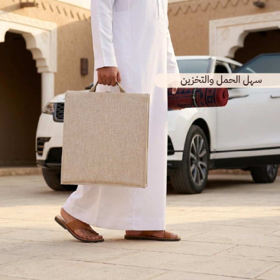 شخص يرتدي ثوب ا أبيض يحمل حقيبة بيج مع ظهور جزء من سيارة وحمل مفرش