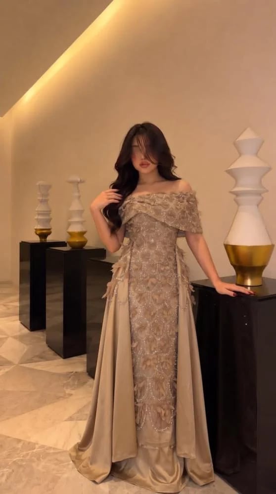 فستان سهرة بيج فاخر بتصميم أوف شولدر مطرز بالكامل بنقوش براقة وزهور ثلاثية الأبعاد مع تنورة درامية وذيل خلفي
