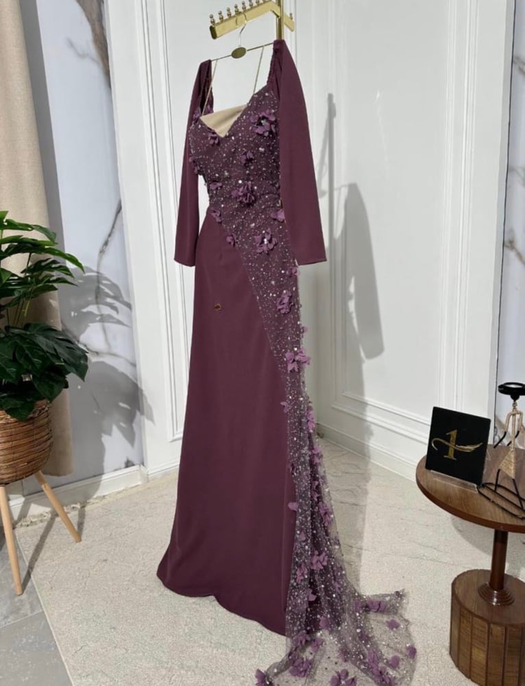 هذا الفستان هو فستان سهرة طويل مصمم من قماش الكريب المريح (ستريتش)، ويتميز بلونه البني الموكي أو الليلكي الغامق.