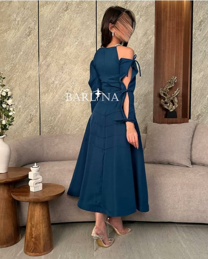 فستان سهرة أنيق بلون تركواز أو بترولي، بتصميم مكشوف الأكتاف (أوف شولدر) مع ياقة مستديرة بسيطة.