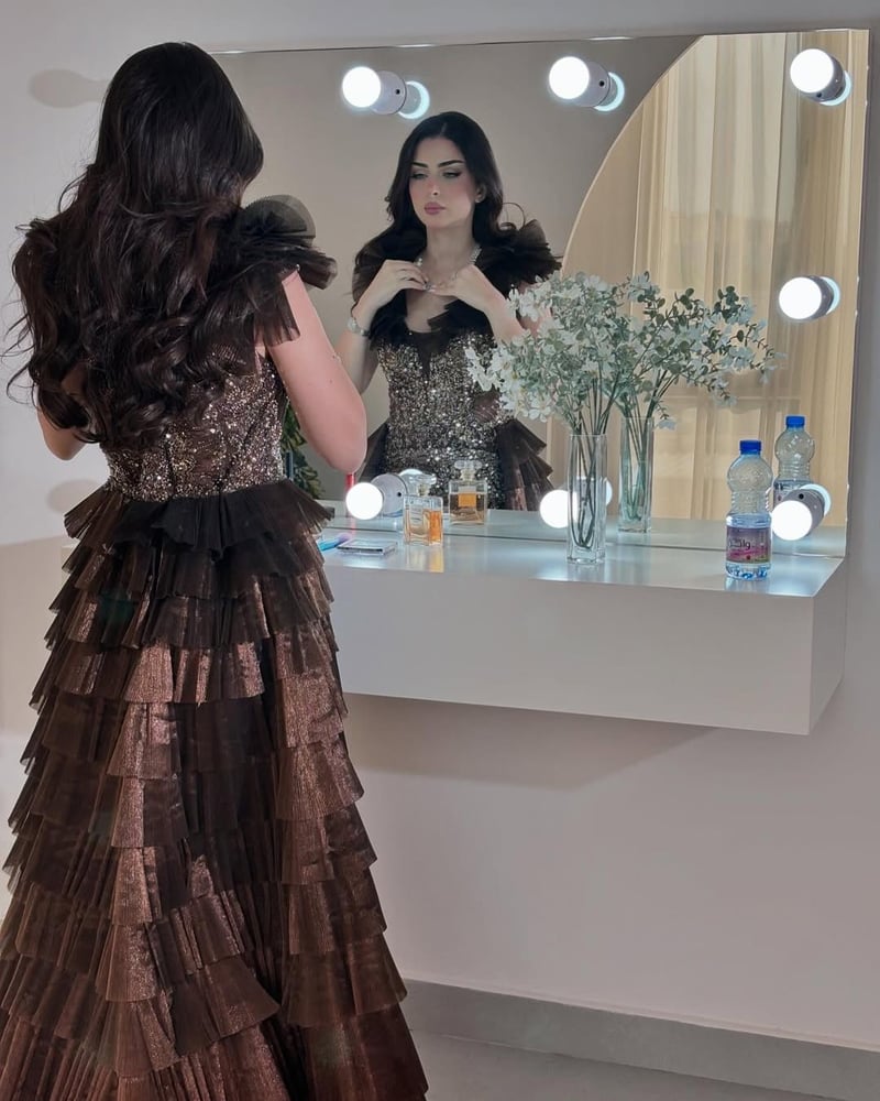 فستان سهرة طويل بلون بني داكن أو برونزي، يتميز بتصميم أنيق وفاخر مع تفاصيل براقة.