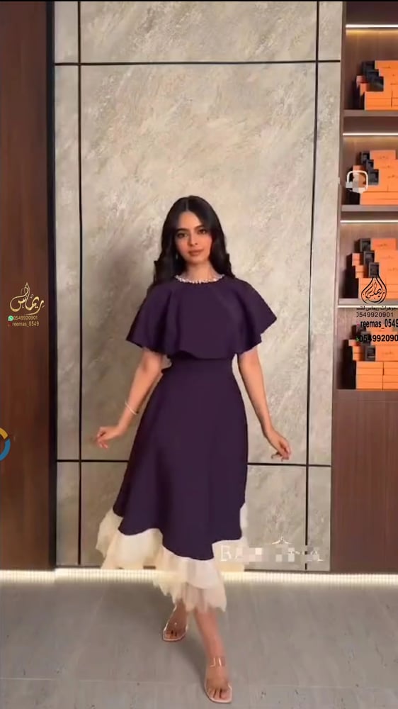 فستان سهرة أنيق بلون داكن (يبدو بنفسجي غامق أو كحلي) مع تفاصيل بيضاء في الجزء السفلي.