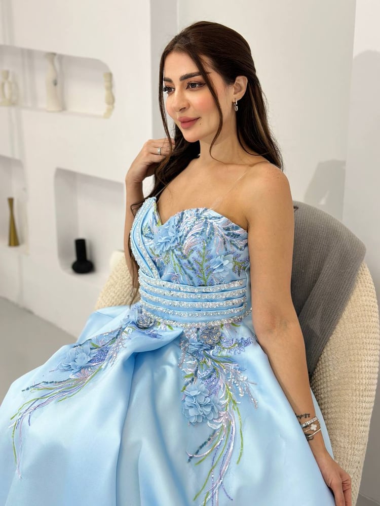 فستان سهرة طويل بلون أزرق سماوي فاتح، يتميز بتصميم أنيق ومفصل بالورود على الصدر وتنورة واسعة