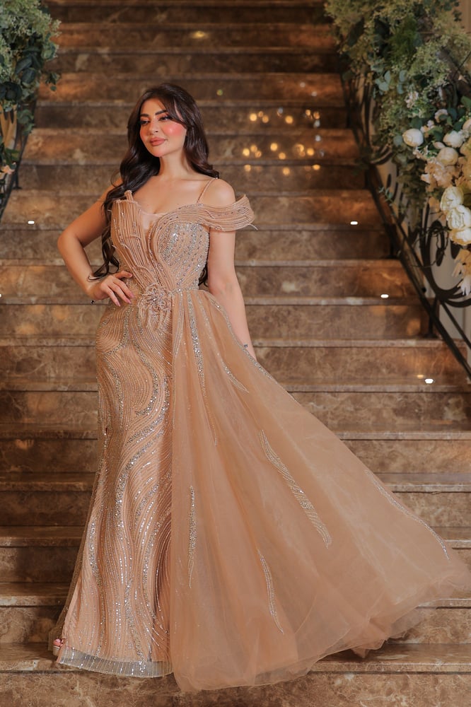 A dress with a luxurious and feminine design, in a soft beige color with a hint of gold, fully decorated with sparkling embroidery in an artistic arrangement that reflects elegance.