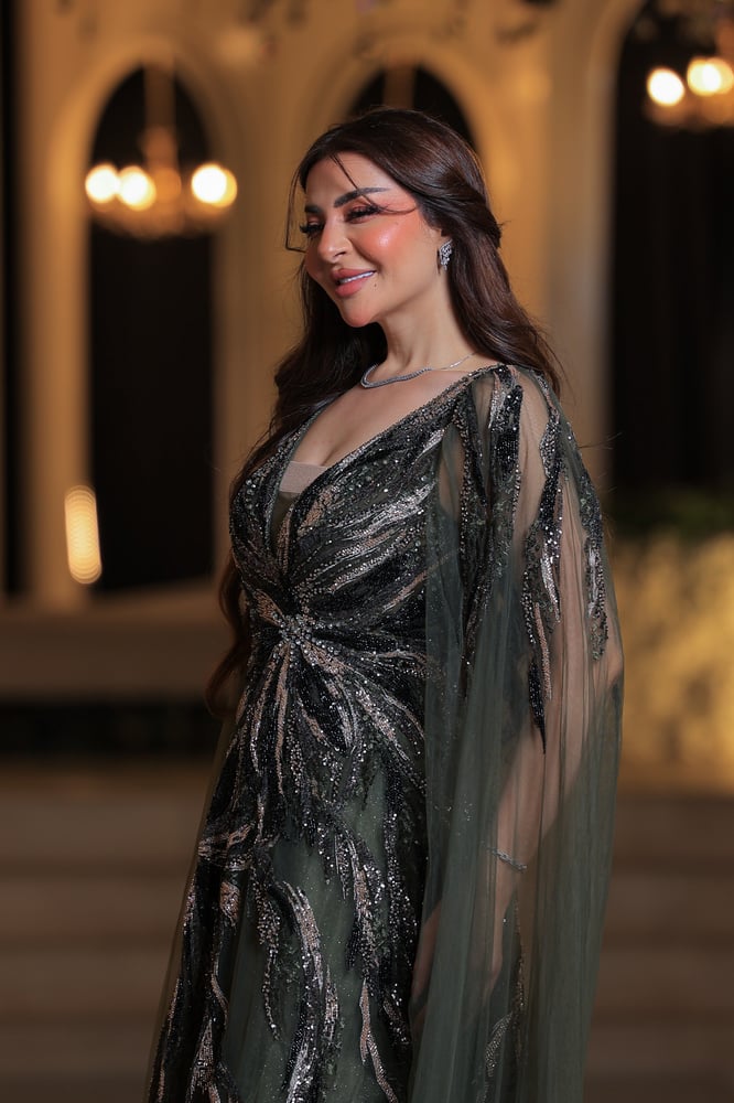 فستان سهرة فاخر وأنيق بتصميم راقٍ جدًا. لون الفستان زيتي ، ومزين بتطريزات لامعة من الخرز والترتر باللون الفضي المائل للذهبي