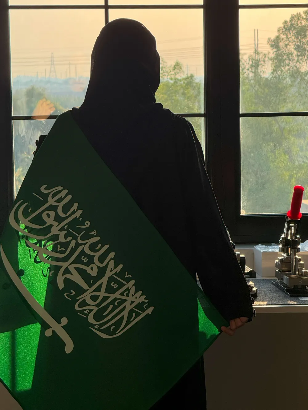 موظفة من ميار ميموريز تحمل العلم السعودي أمام نافذة الاستوديو